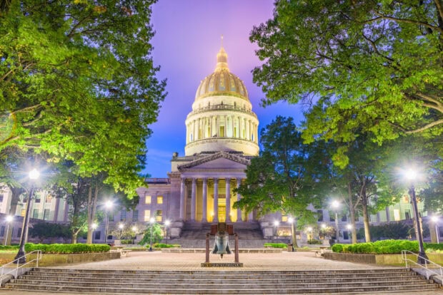 The West Virginia State Capitol building surrounded by green trees at dusk in West Virginia