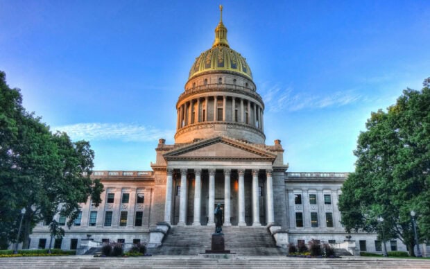 The West Virginia state capitol building with a golden dome surrounded by trees under a clear blue sky