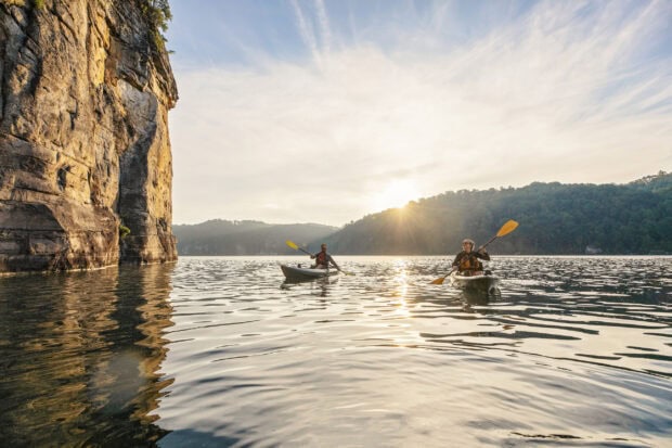 Two people kayaking near a cliff in West Virginia during sunset
