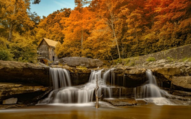 A wooden mill beside a waterfall surrounded by autumn foliage in West Virginia