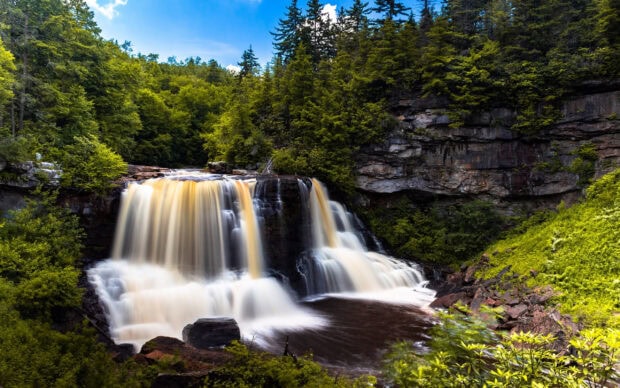 Beautiful waterfall in West Virginia surrounded by lush green forest and rocky cliffs