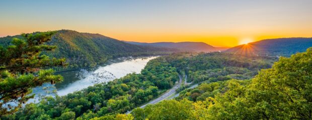 A scenic view of West Virginia hills and river at sunset with lush green forests