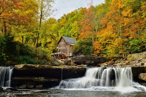 Historic mill in West Virginia surrounded by colorful autumn trees and flowing waterfall