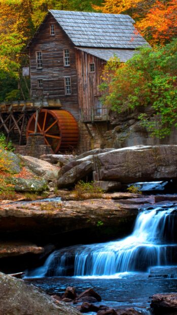 Historic West Virginia grist mill with vibrant autumn foliage and flowing waterfall