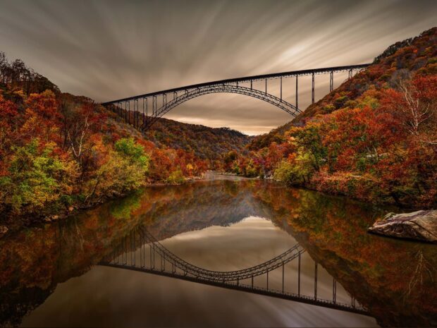 Autumn foliage and arch bridge reflecting over river in West Virginia landscape