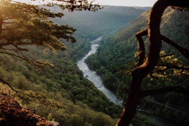 A scenic view of West Virginia river winding through lush forested mountains at sunset