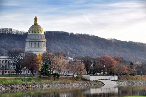 The West Virginia capitol building is surrounded by autumn trees near the calm river