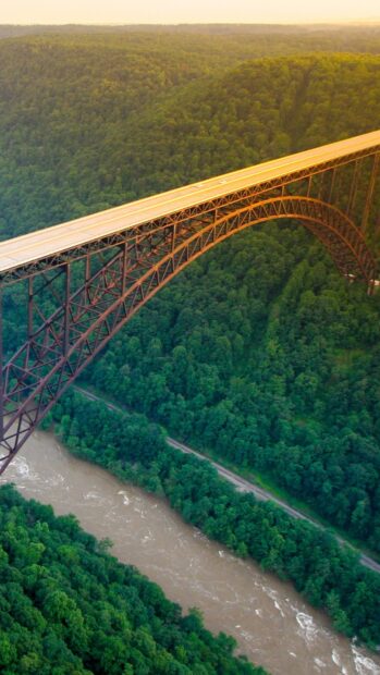A stunning view of West Virginia with a large steel arch bridge over a river surrounded by dense forest