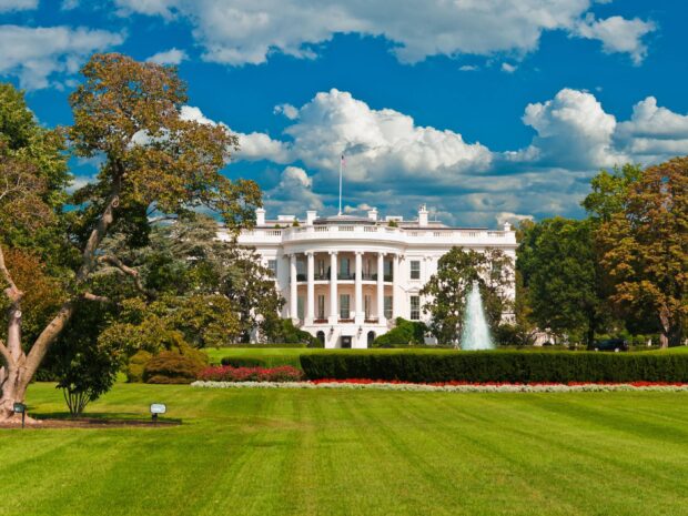 The White House surrounded by green trees and a clear blue sky with white clouds