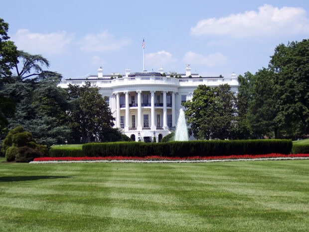 The White House with a large green lawn and a fountain in front under a blue sky