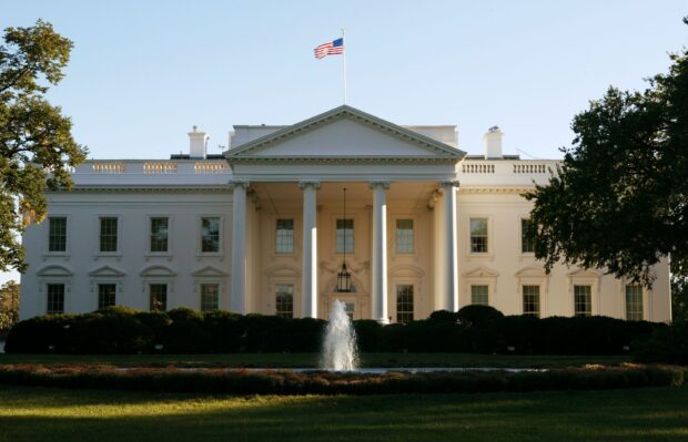 The White House with American flag and fountain in front surrounded by trees and bushes