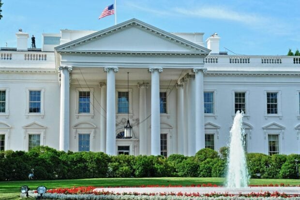 The White House with American flag and water fountain in front of lush green garden