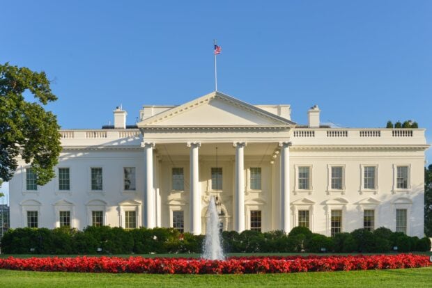 The White House is surrounded by lush gardens and a bright blue sky