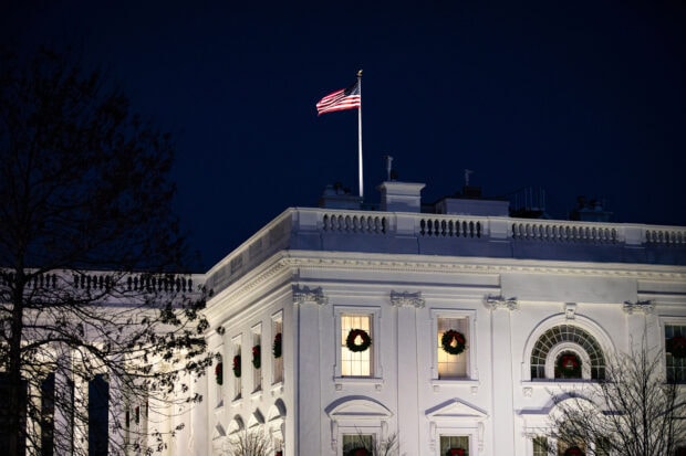 White House at night decorated with wreaths and an American flag on top