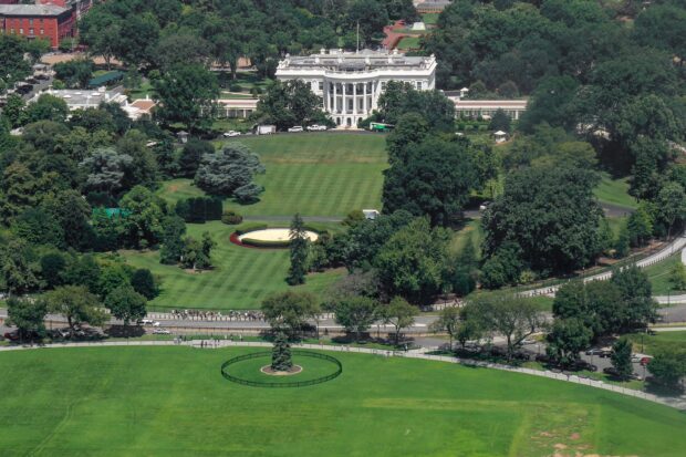 Aerial view of the White House surrounded by lush green gardens and trees