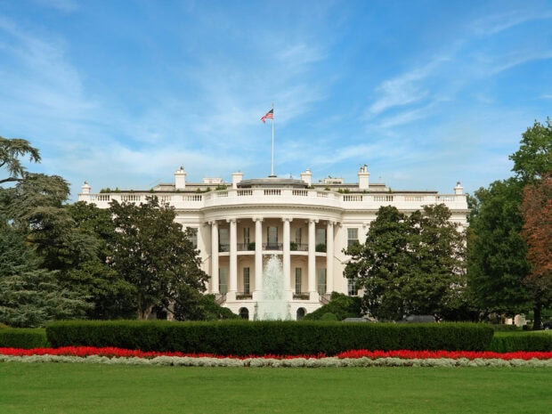Front view of the White House with trees and a fountain under a clear sky