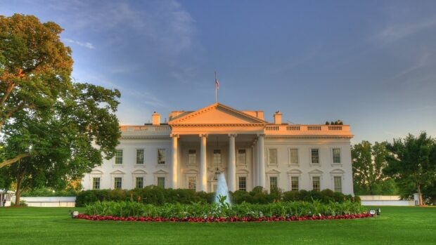 The White House building surrounded by green trees and a fountain in front at sunset