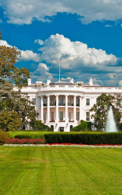 A clear view of White House with lush green lawn and vibrant flowers under a bright sky