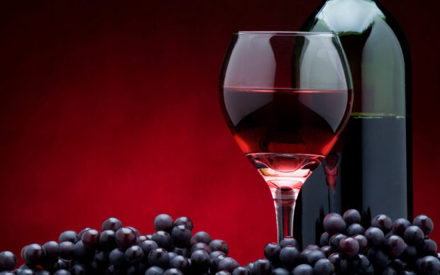 Red grapes beside a wineglass filled with red wine and a wine bottle on a red background