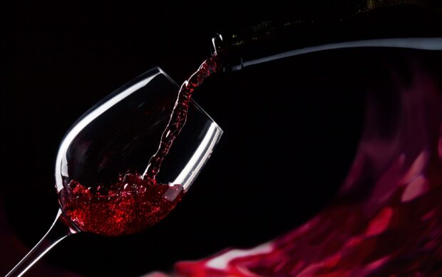 Red wine glass being filled with wine in a close up view against a dark background