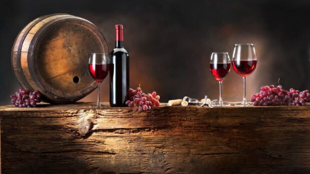 Red wineglass with grapes and wine barrel on rustic wooden table