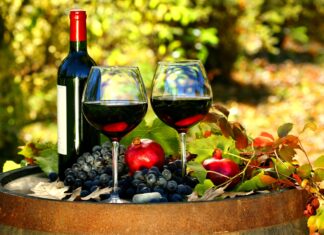 Two wineglass with red wine beside grapes and pomegranates on a wooden barrel outdoors