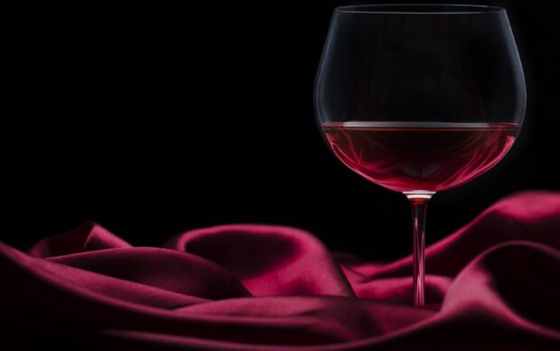 A wineglass filled with red wine on a red silk cloth with a black background