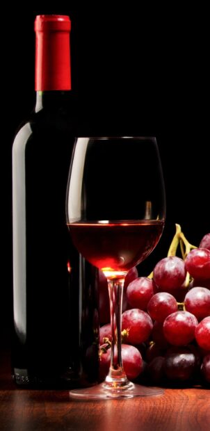 Red wineglass with grapes and bottle on wooden table