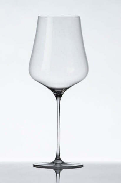 A clear empty wineglass with a long stem standing on a reflective surface