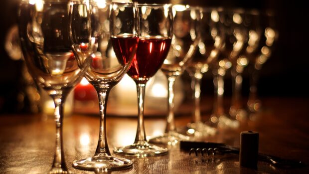 A row of wineglass with one filled with red wine on a wooden table with warm lighting