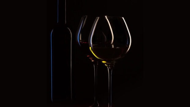 A wineglass with white wine and a wineglass with red wine beside a dark wine bottle