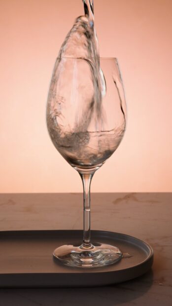 Clear water flowing into a wineglass on a tray in a close up view