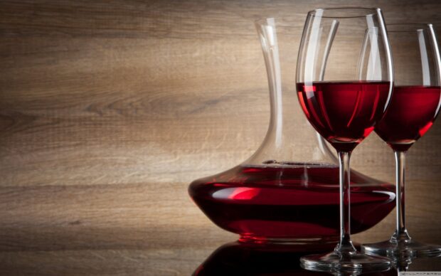 A decanter and two wineglass filled with red wine on wooden surface