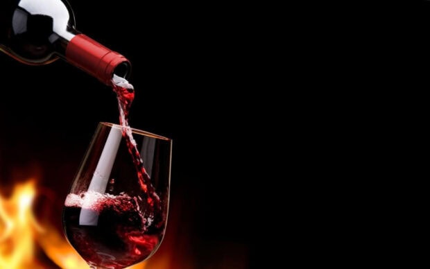 Red wine being poured from bottle into glass near fire light