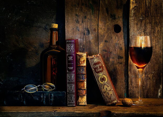 A vintage wineglass and bottle displayed with classic books on a rustic wooden surface