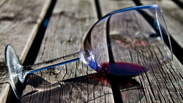 A wineglass resting on a wooden surface with a small amount of wine inside