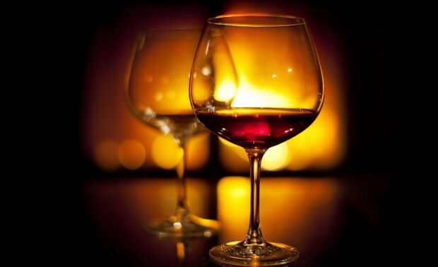 A wineglass with red wine in a warm glowing setting with another empty wineglass in the background