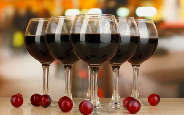 Five wineglass filled with red wine and fresh grapes placed on table