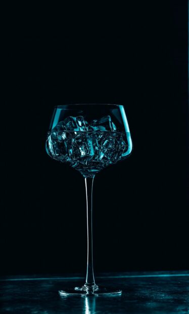 Clear wineglass filled with ice cubes on a dark background
