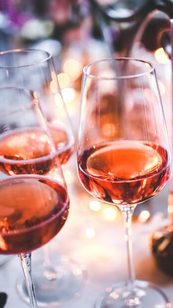 Close up of wineglass filled with rose wine in a party setting with lights in background