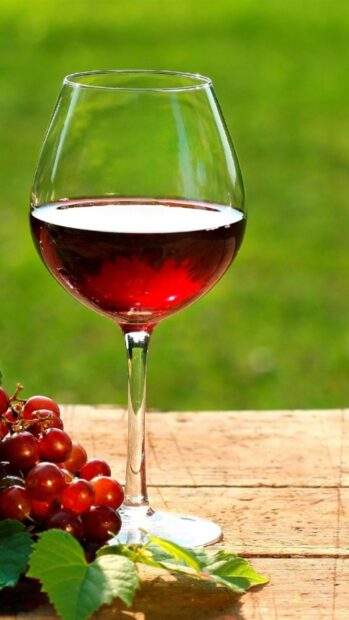 A wineglass filled with red wine beside fresh grapes on a wooden surface