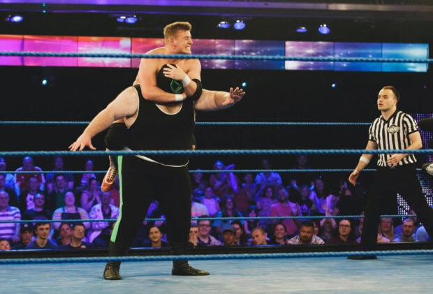 A wrestling competitor lifting his opponent in a wrestling ring during a live match