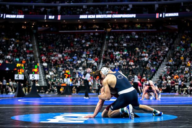 College wrestling match shows two athletes competing intensely on the mat in front of a large audience