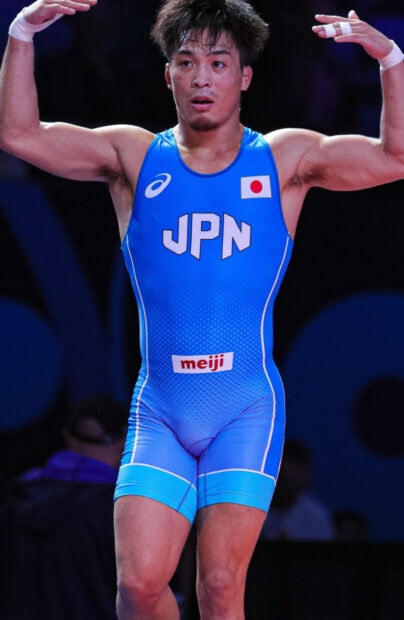 Male wrestler in blue singlet representing Japan raising his arms on the mat