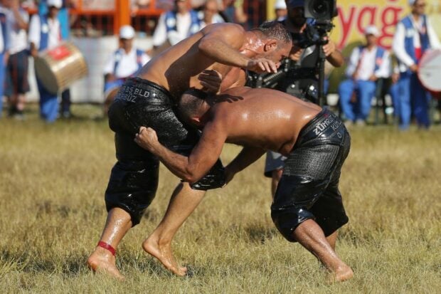 Two wrestlers in traditional leather pants grappling intensely during an outdoor wrestling match