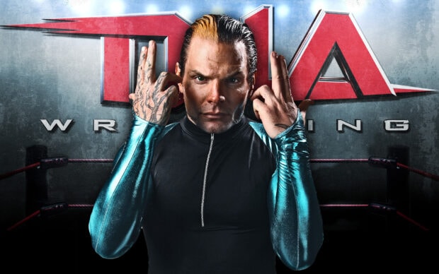 A wrestler with tattooed hands posing in front of a wrestling logo