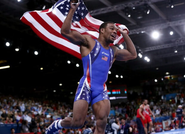 A wrestler celebrating victory holding the American flag during a wrestling match in a stadium
