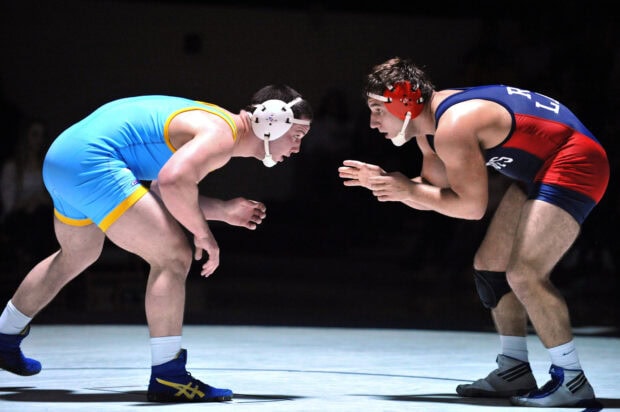 Two wrestlers competing on the mat in a wrestling match with headgear and singlets
