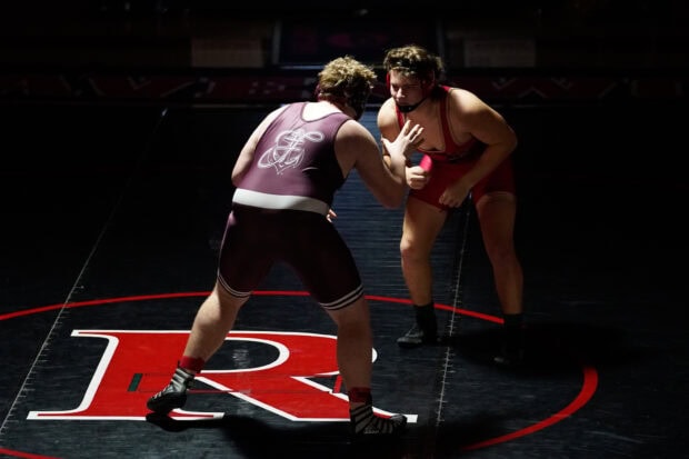 Two wrestlers preparing to grapple on a dark mat with a red letter r in the center