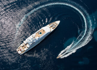 A luxury yacht cruising in the deep blue sea with a speedboat creating a curved trail behind